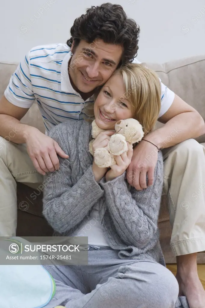 Mid adult woman hugging a stuffed animal with a mid adult man behind her