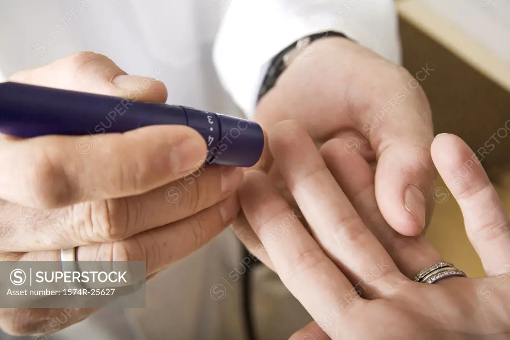 Mid section view of a male doctor taking a blood sample from a patient's finger