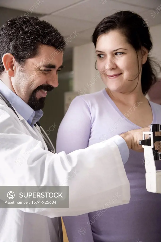 Male doctor measuring the weight of a patient and smiling