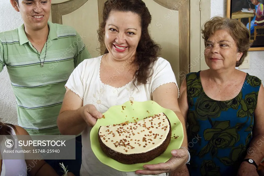 Mature woman holding a cake on a plate with a young man and a mature woman standing beside her
