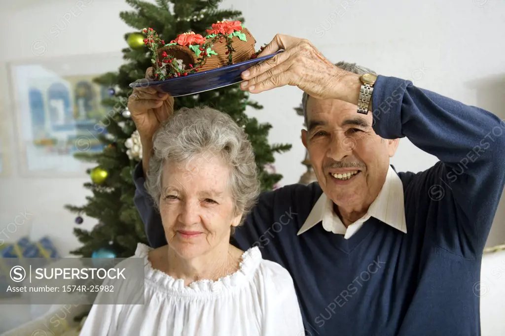 Portrait of a senior man holding a plate of Yule log shaped cake over a senior woman's head