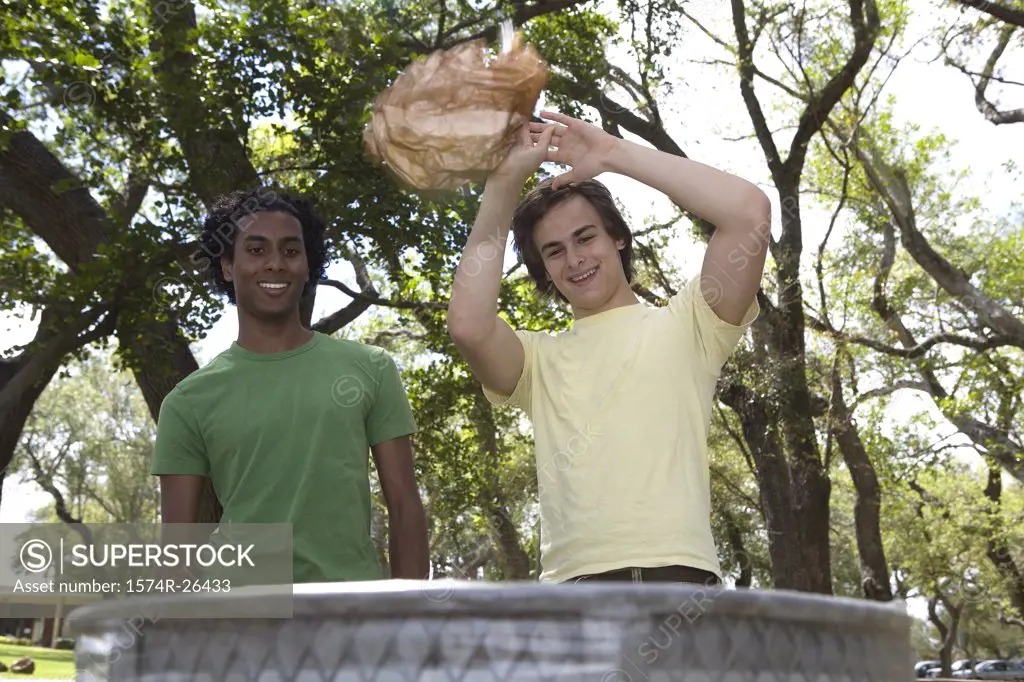 Two young men throwing trash in a garbage can