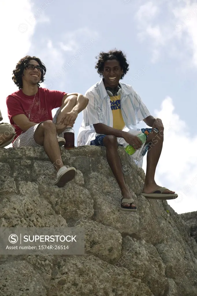 Low angle view of two young men sitting on a rock