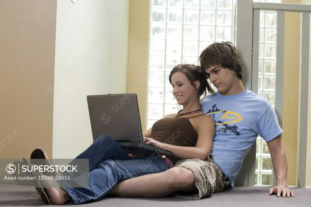 Young man sitting behind a teenage girl using a laptop