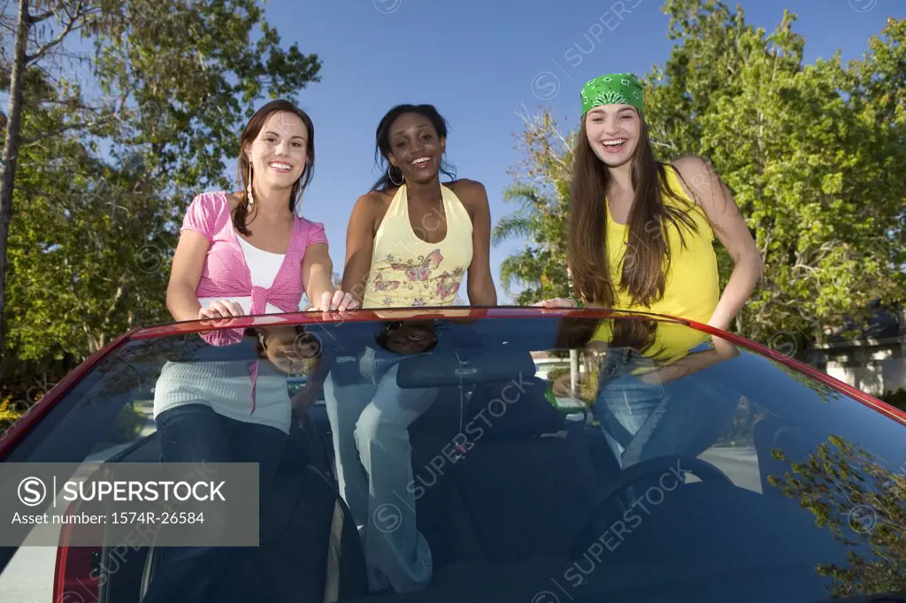 Two teenage girls and a young woman standing in a convertible car