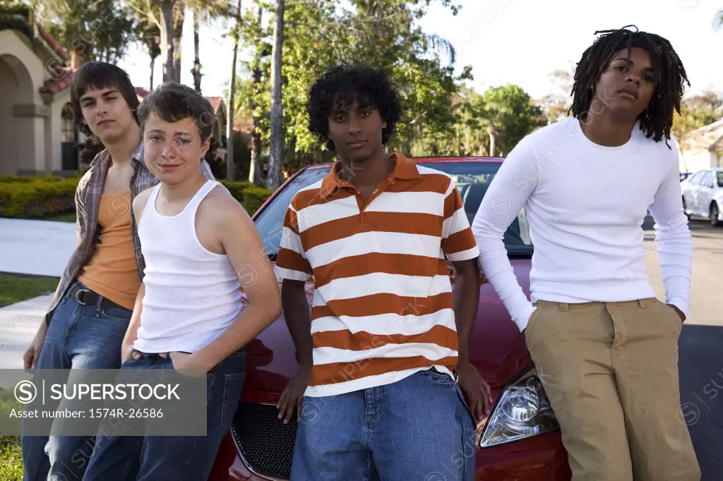 Two teenage boys and two young men leaning against a car