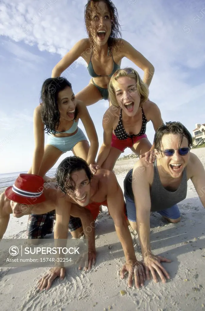 Low angle view of a group of young men and women making a pyramid on the beach