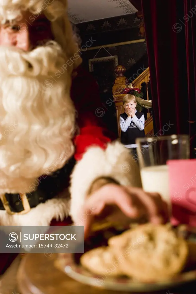 Santa Claus reaching for a cookie with a boy watching in the background