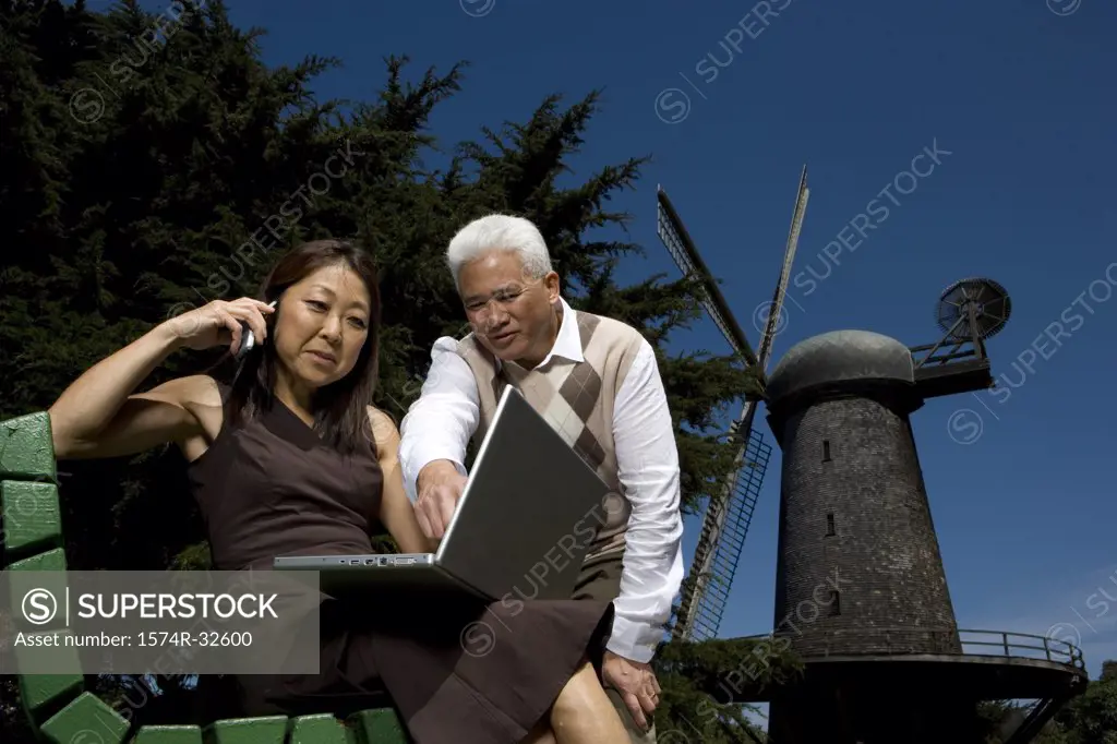 Low angle view of a mature woman talking on a mobile phone with a mature man standing beside her, Golden Gate Park, San Francisco, California, USA