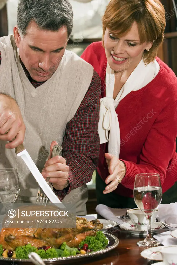 Mature man carving a roast turkey with a mature woman watching