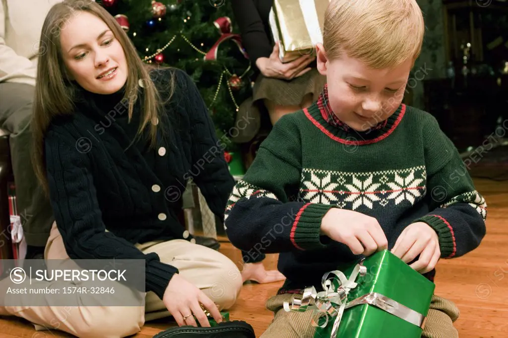 Boy opening a Christmas present with his mother behind him