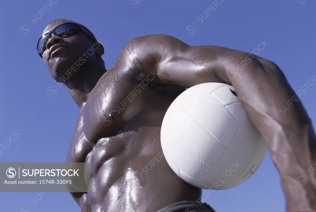 Low angle view of a young man standing holding a volleyball