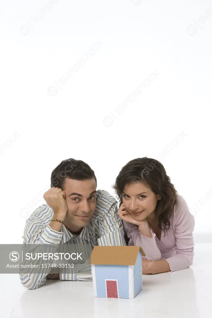 Young couple lying behind a model of a home