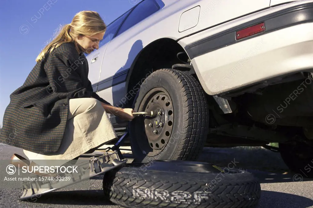 Side profile of a young woman changing tire of a car