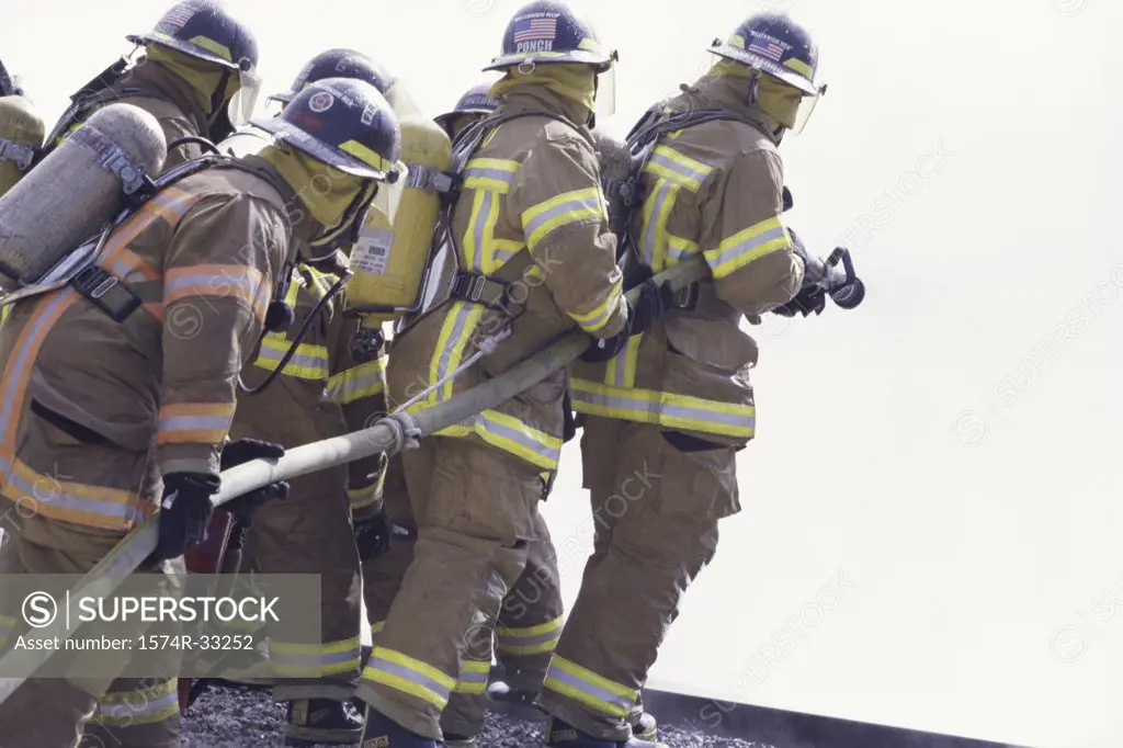 Side profile of a group of firefighters holding water hoses