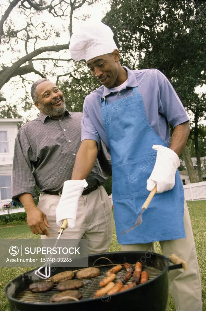 Young man barbecuing with his father standing beside him