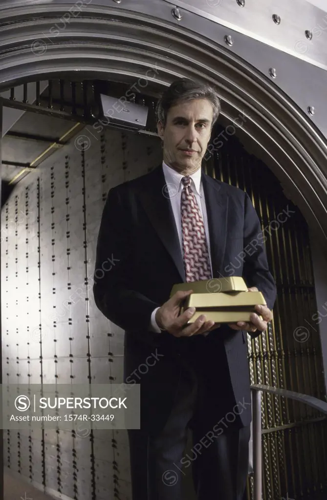 Businessman standing in front of a vaulted door and holding gold bars