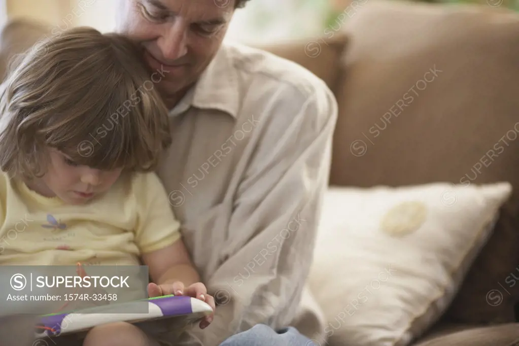 Close-up of a girl sitting on her father's lap and writing on a slate