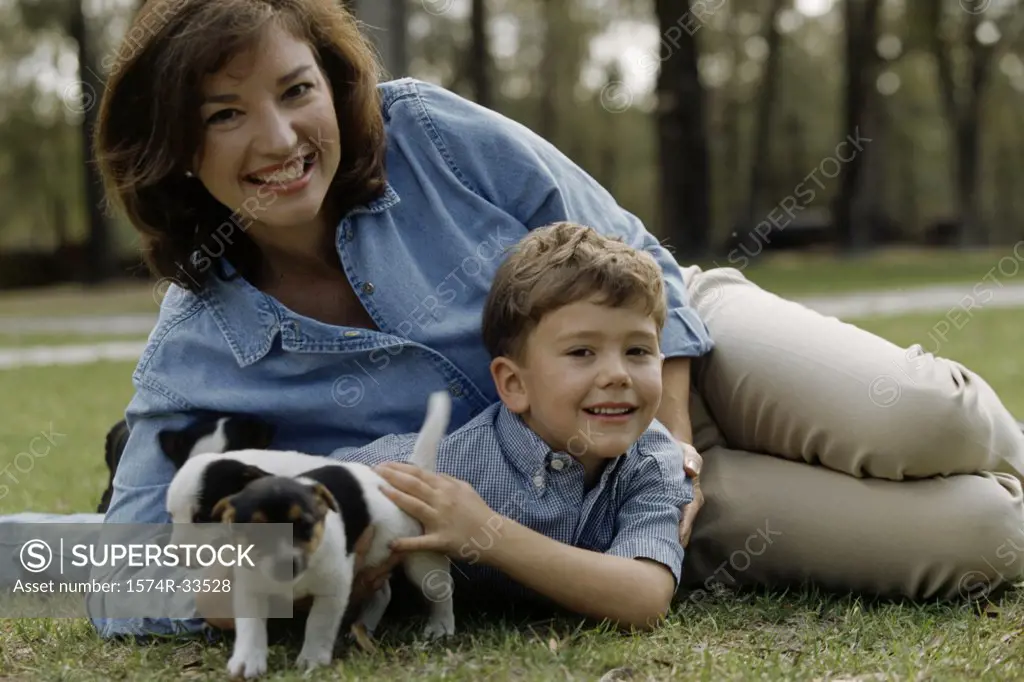 Portrait of a mid adult woman and her son playing with three puppies in a park
