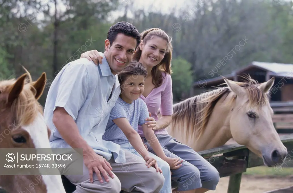 Portrait of parents with their daughter sitting on the fence of a stable