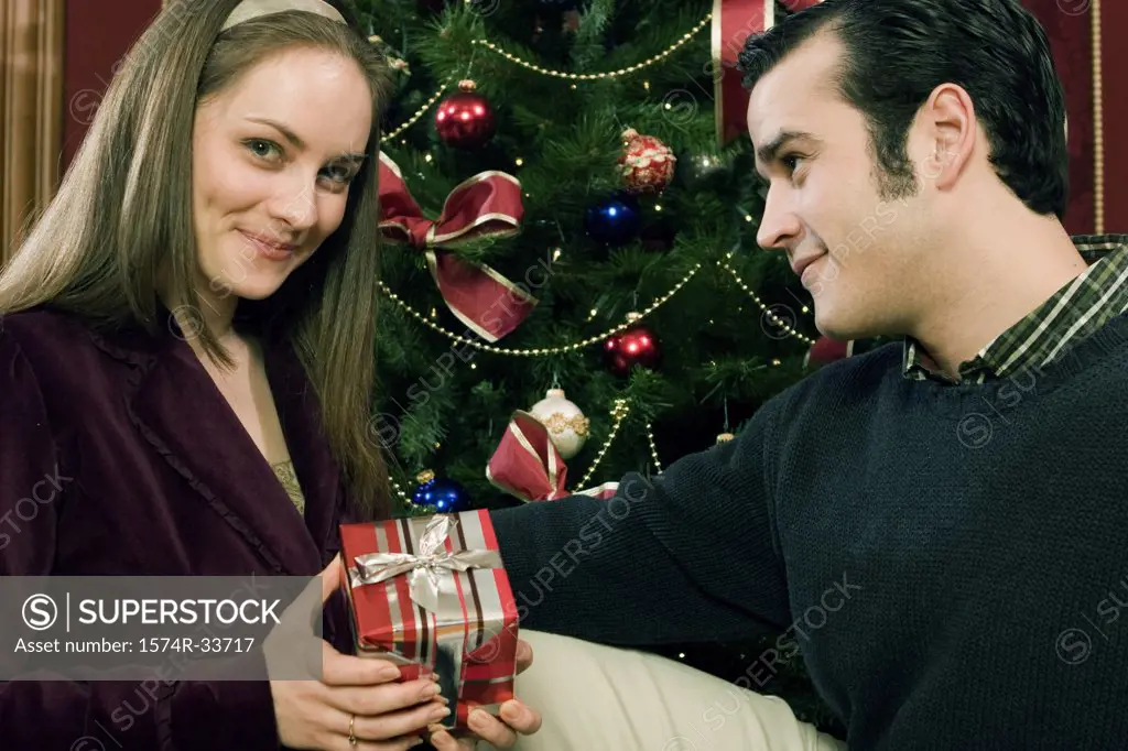 Young woman holding a Christmas present and sitting with a young man