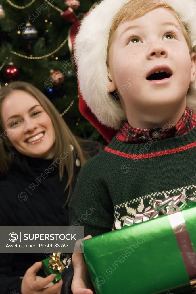 Boy holding a Christmas present with his mother behind him