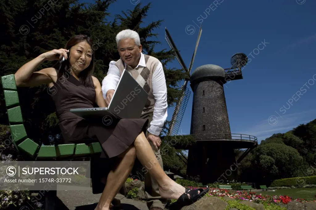 Low angle view of a mature woman talking on a mobile phone with a mature man standing beside her, Golden Gate Park, San Francisco, California, USA