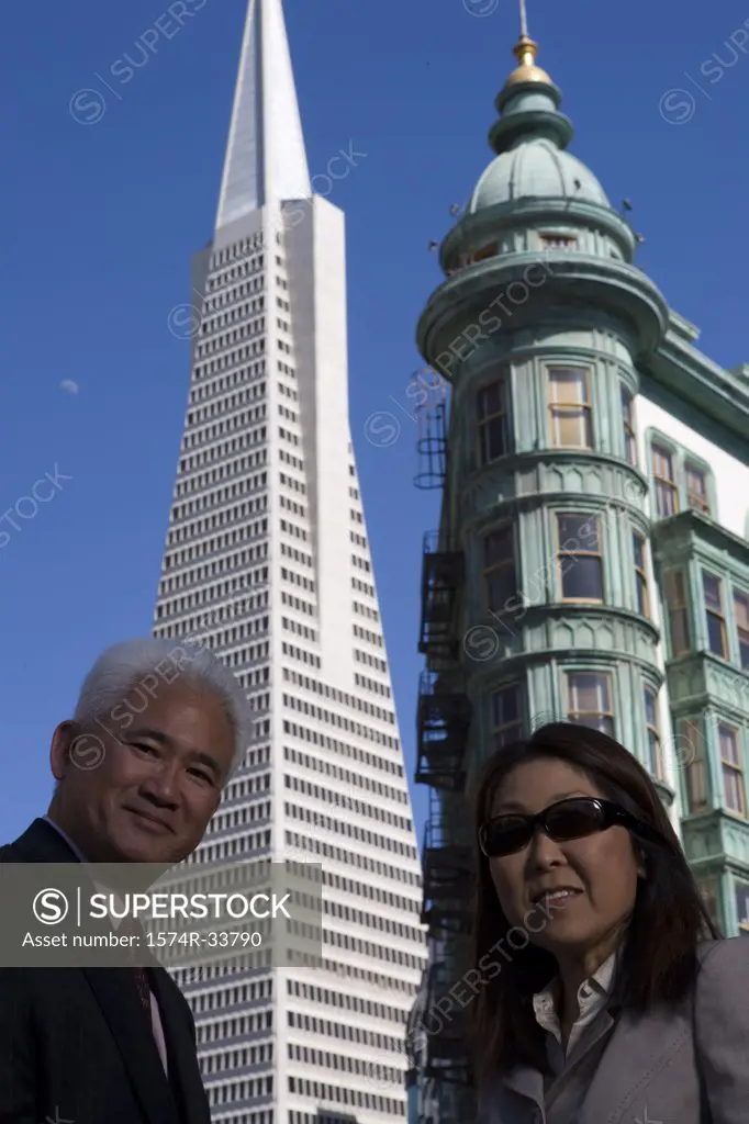 Low angle view of a businessman and a businesswoman standing in front of buildings, Transamerica Pyramid and Columbus Tower, San Francisco, California, USA