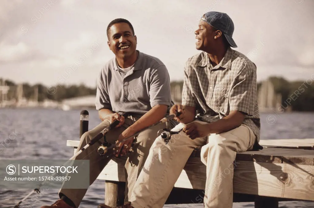 Mature man sitting with his teenage son on a pier fishing