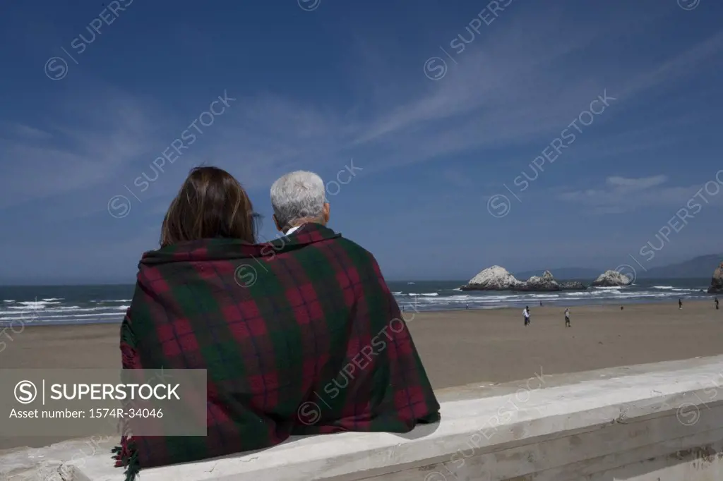 Rear view of a mature couple wrapped in a blanket on the beach