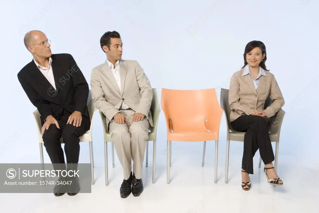 Two businessmen looking at a businesswoman sitting in a chair
