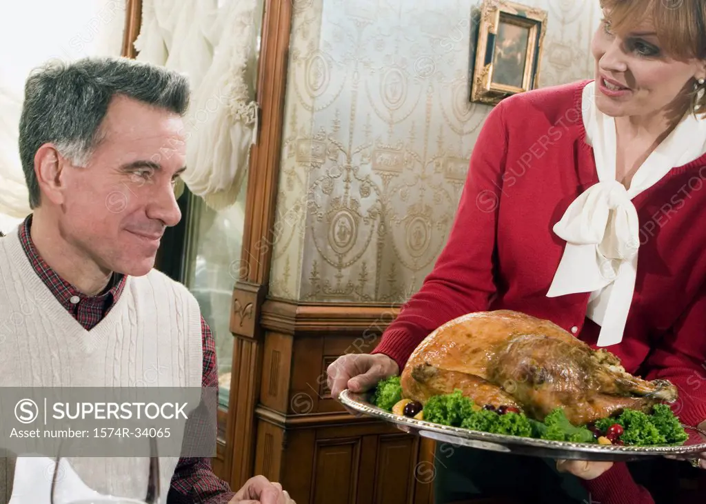 Mature woman carrying a roast turkey with a mature man watching
