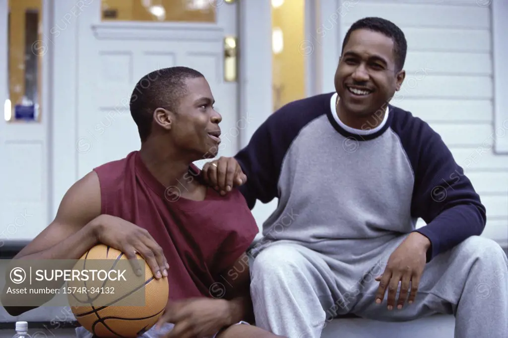 Mature man sitting with a teenage boy holding a basketball