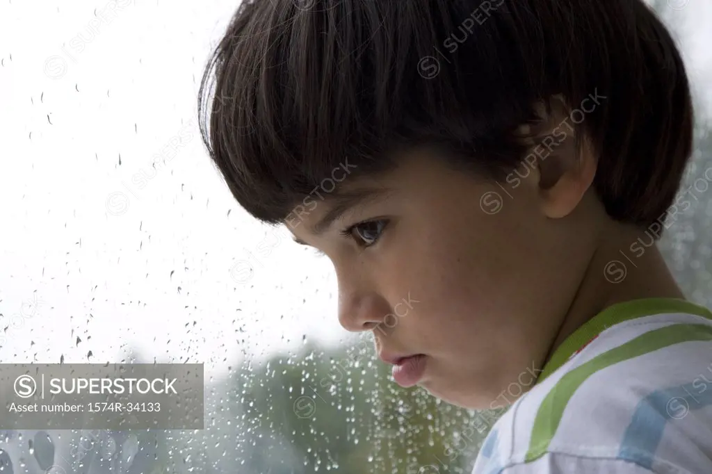 Close-up of a boy looking out a window on a rainy day