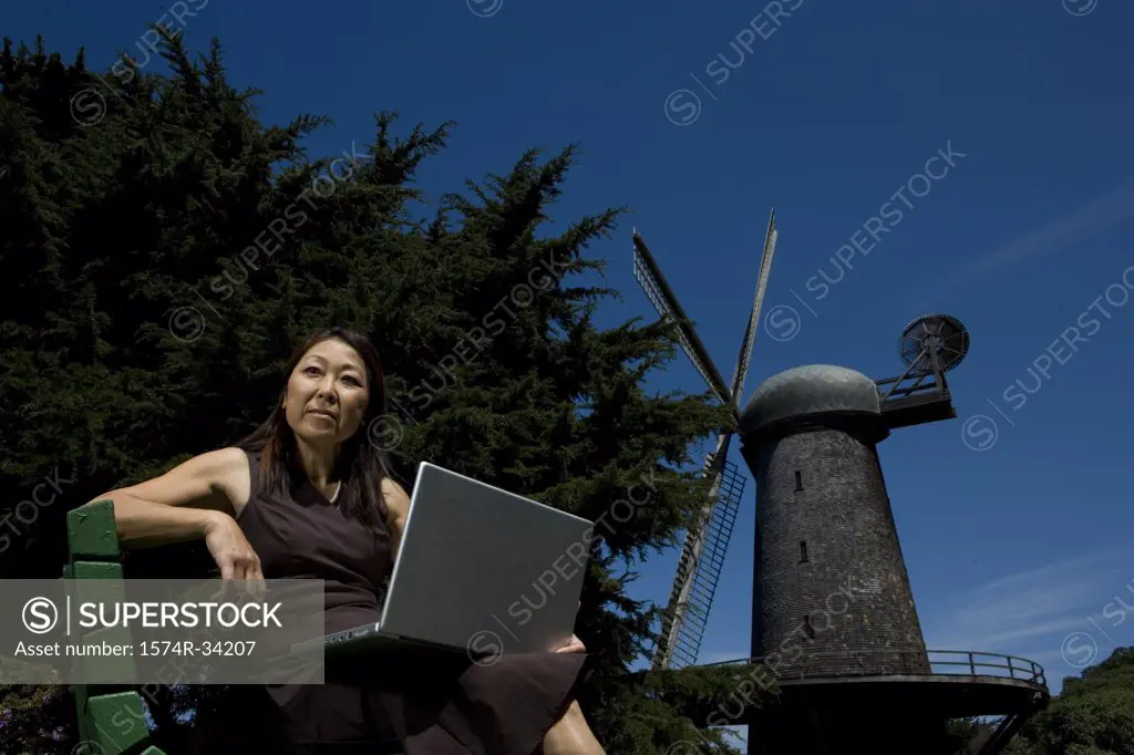 Low angle view of a mature woman sitting on a bench with a laptop on her lap, Golden Gate Park, San Francisco, California, USA