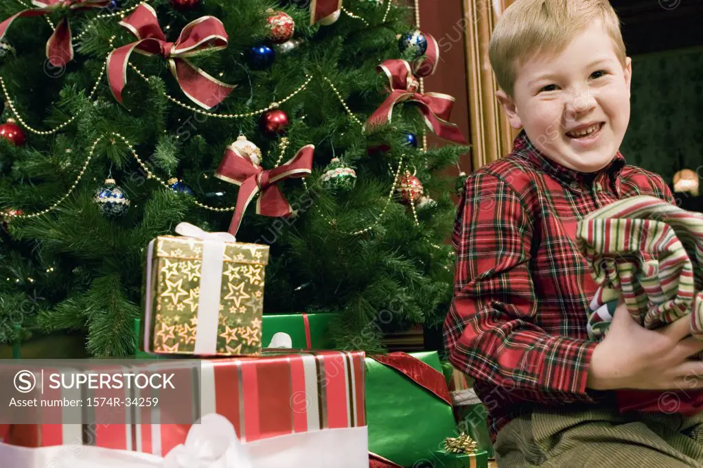 Boy in front of a Christmas tree holding wrapping paper