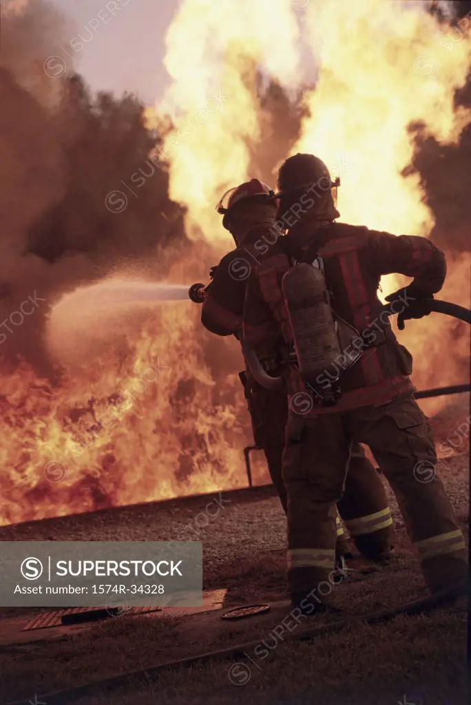 Rear view of two firefighters extinguishing fire