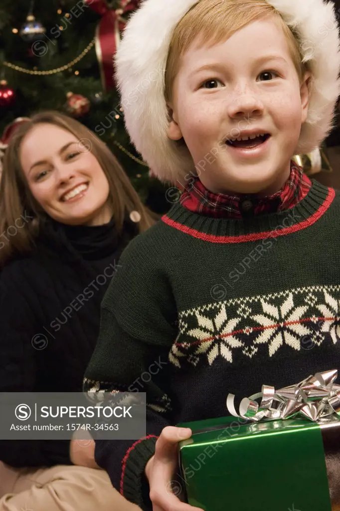 Boy holding a Christmas present with his mother behind him