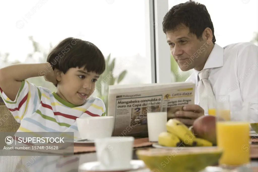 Close-up of a mature man reading a newspaper with his son at a breakfast table