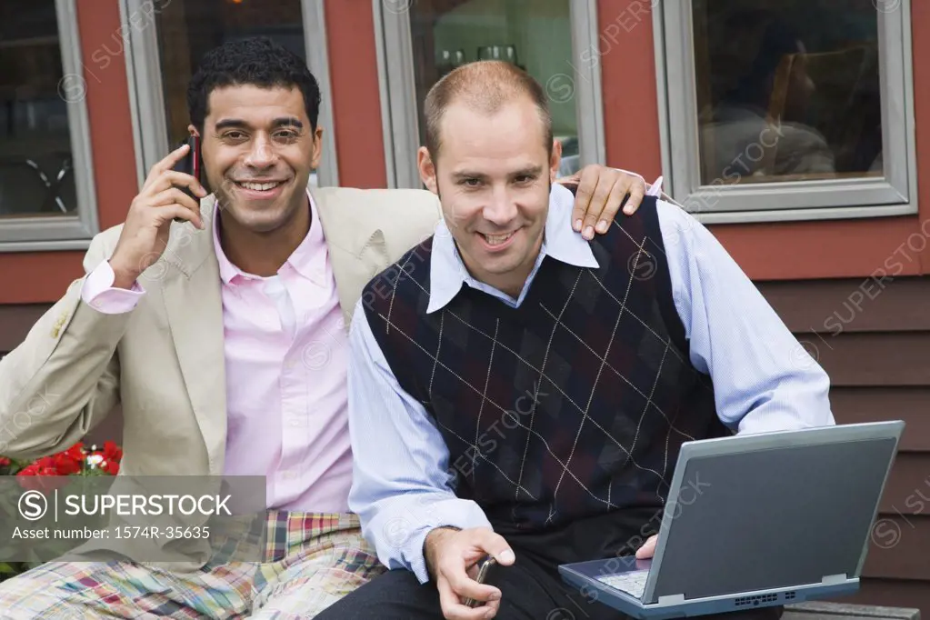 Businessman talking on mobile phone with another businessman sitting beside him