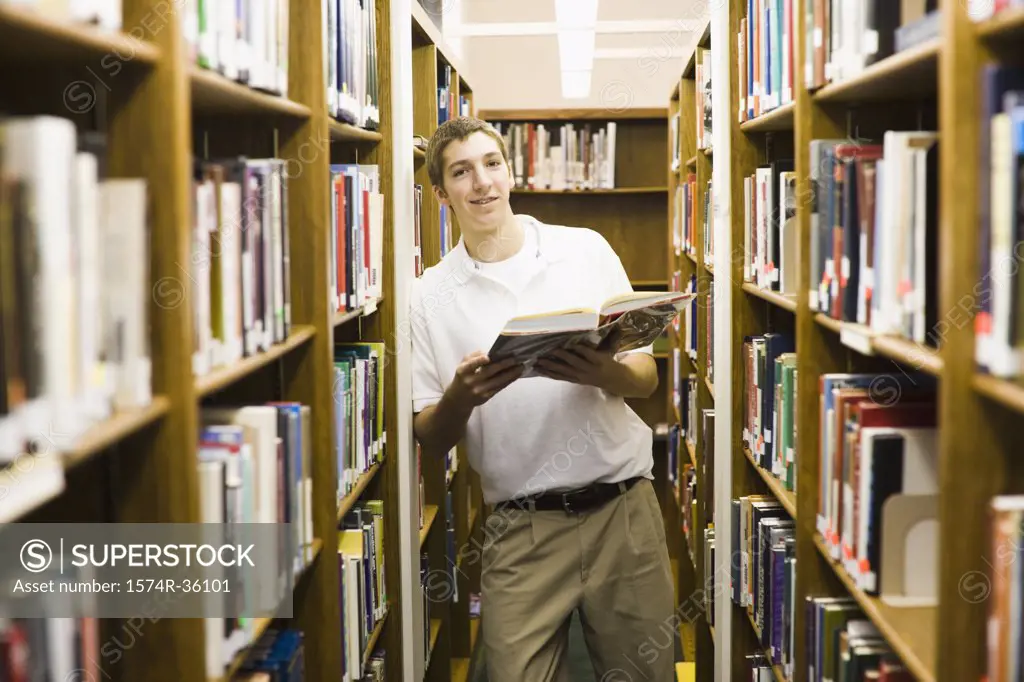 Student holding a book and standing in a library