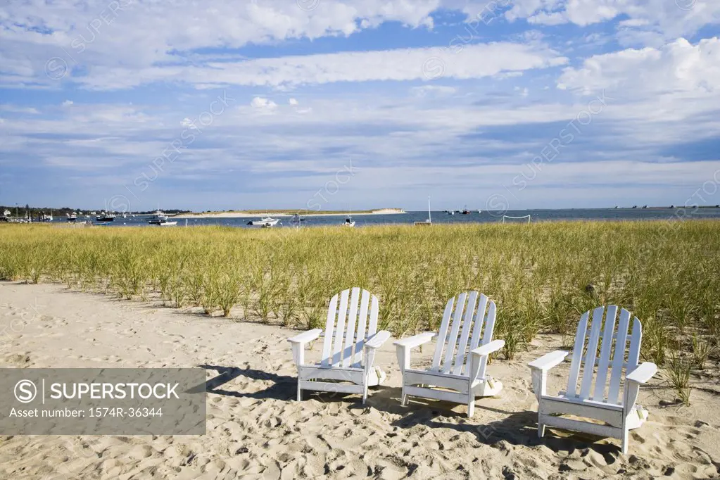 Three empty adirondack chairs on the beach