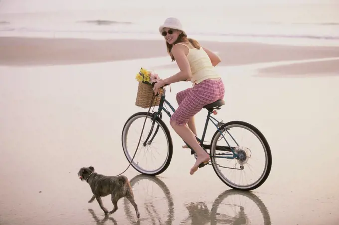 Portrait of a young woman riding a bicycle with her dog running alongside