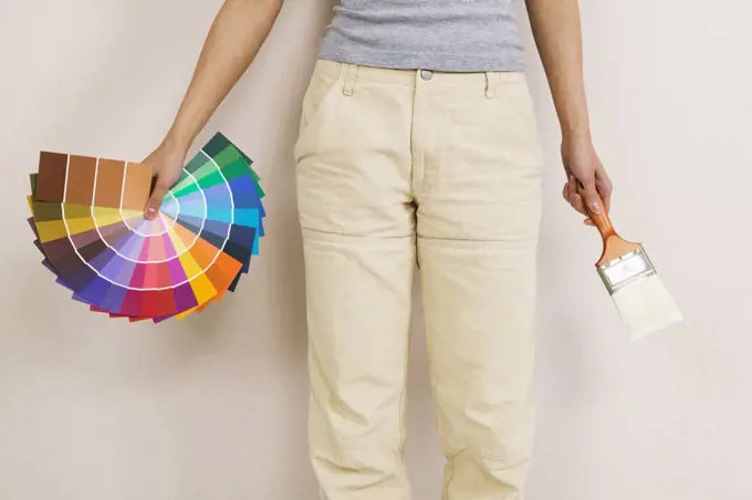 Mid section view of a woman holding color swatches and a paintbrush
