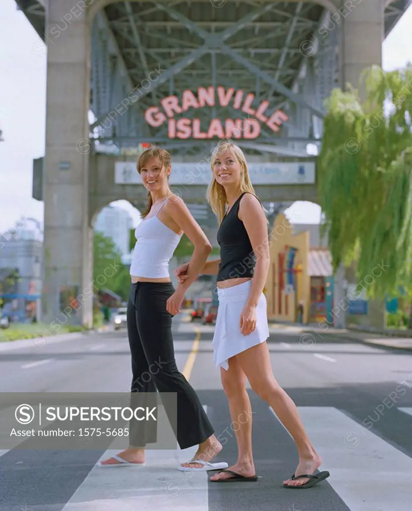 Two women walking across a cross_walk with Granville Island sign behind them _ Vancouver BC