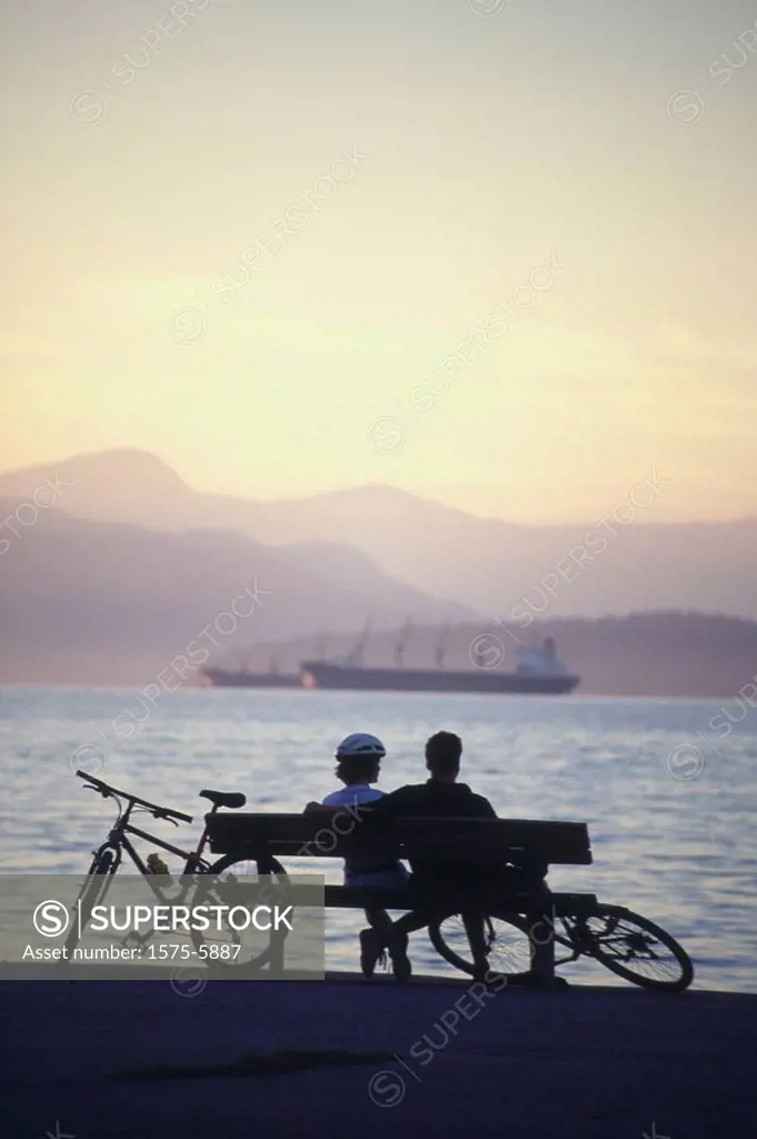 Silhouette of couple sitting on bench with bikes at Kit´s Beach, Vancouver, BC, Canada