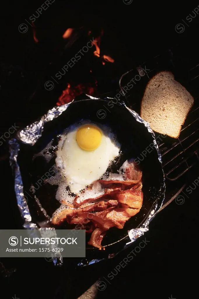 Camp breakfast over open flame, bacon and eggs.