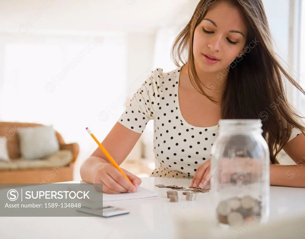 Indian woman counting coins and writing on notepad