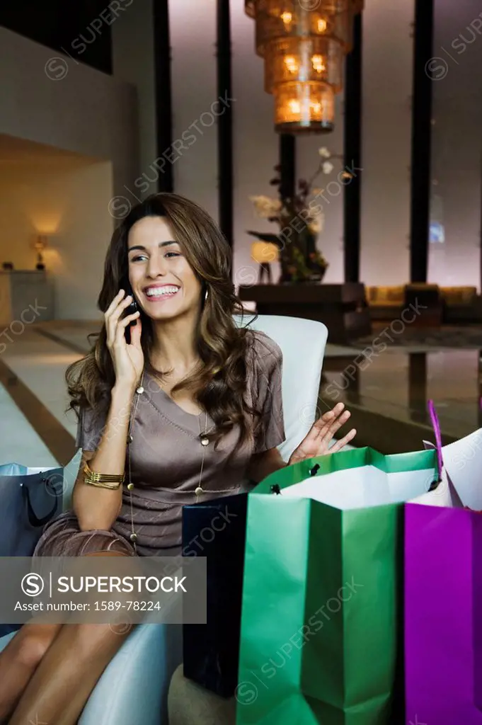 Hispanic woman talking on cell phone and surrounded by shopping bags