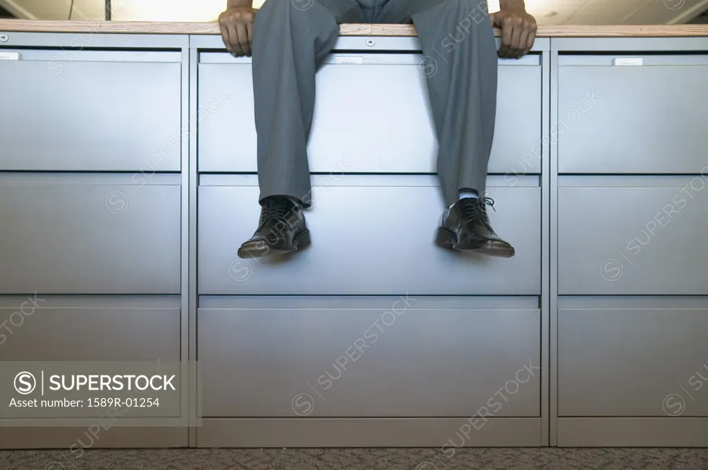 Businessman sitting on a filing cabinet